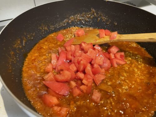 煮詰めたミートソースにさいの目切りにしたトマトを入れる